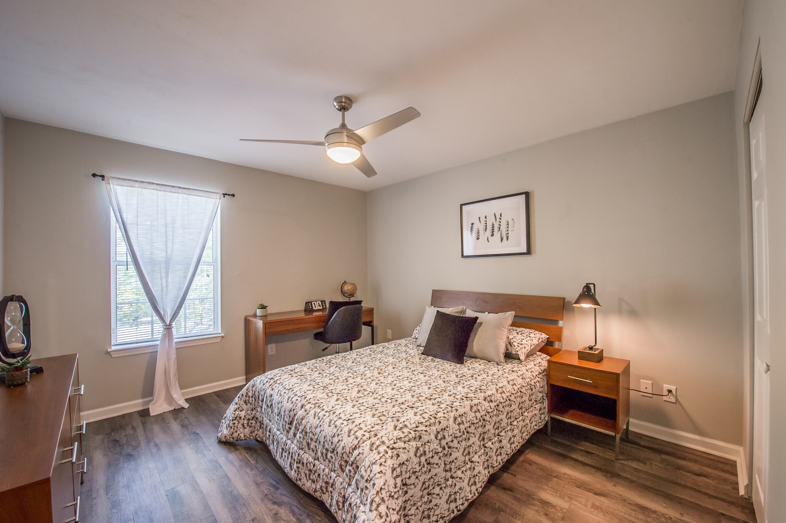 Model bedroom with windows, bed, fan and night stand at Elevate Apartments in Tallahassee, FL